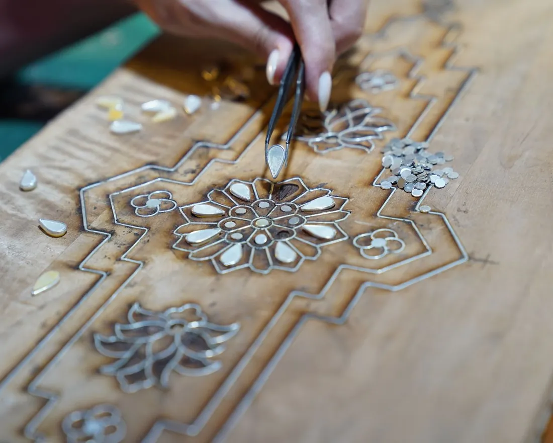 Manos colocando con pinzas piezas menudas de un dibujo embutido sobre un tablero de madera clara